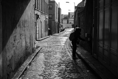 Rear view of woman walking on footpath amidst buildings