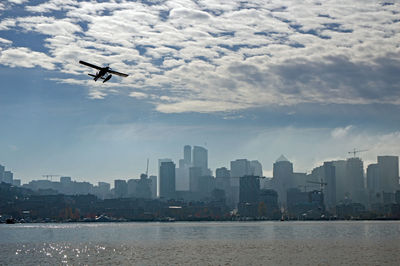 Scenic view of lake by buildings against sky with plane