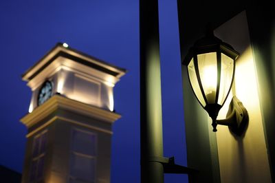 Low angle view of lamp mounted on wall by bell tower at night