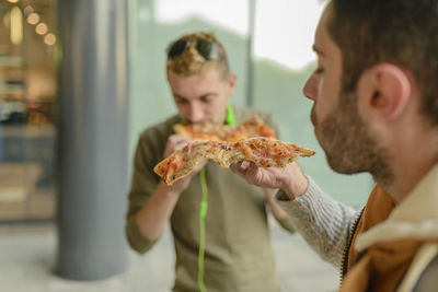 Male friends eating pizza while standing in city