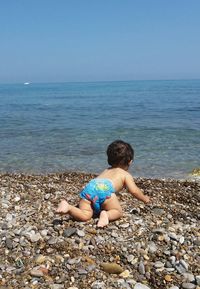 Baby crawling at beach against clear blue sky