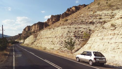 Cars on road by rock formation against sky
