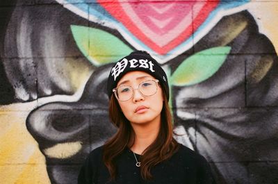 Portrait of beautiful young woman standing against graffiti wall