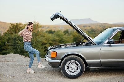 Side view of young woman standing in car