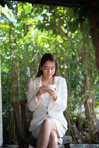 Businesswoman drinking coffee while sitting on chair against trees