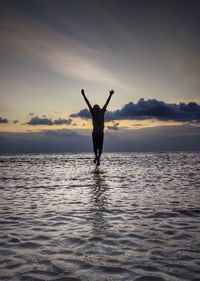 Silhouette man standing in sea against sky during sunset