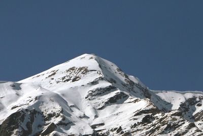 Low angle view of snowcapped mountains against clear blue sky