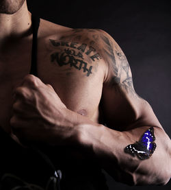 Cropped image of muscular man with tattoos against black background