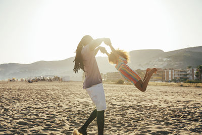 Playful father lifting daughter at beach on sunny day