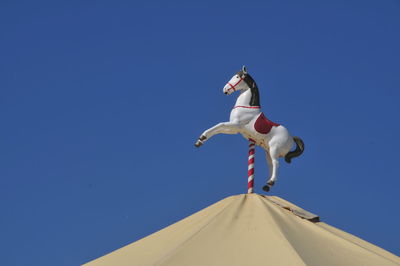 Low angle view of carousel against clear blue sky