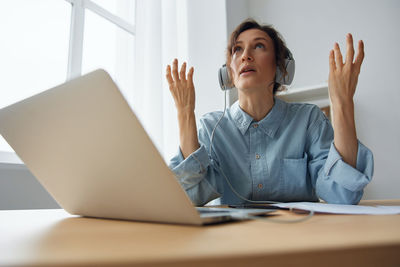 Businesswoman talking through wireless headphones sitting with laptop at office