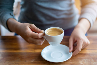 Midsection of woman holding coffee at table