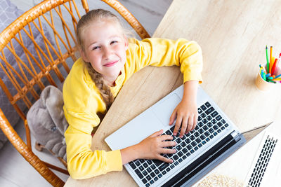 Caucasian girl 10-11 years, hands on laptop keyboard, squinting eyes, top view.