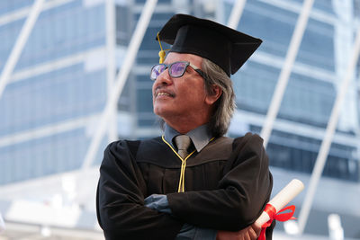 Businessman in graduation gown standing against office building