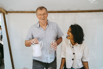 Happy woman looking at senior man holding pitcher in stall at flea market