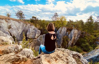 Rear view of woman sitting on rock against sky