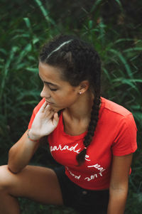 Young woman looking away while sitting on land