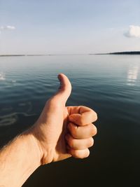 Cropped hand of man gesturing thumbs up sign against sea