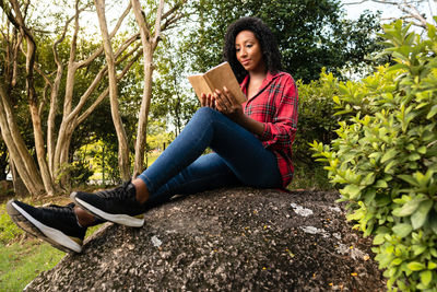 Young woman using mobile phone while sitting against plants