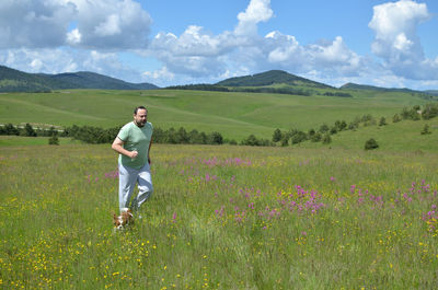 Man and his dog running in a field with wildflowers on a cloudy day in springtime