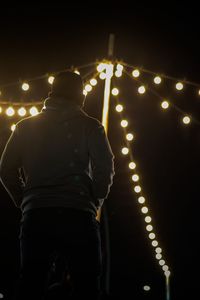 Rear view of man standing against illuminated lights at night