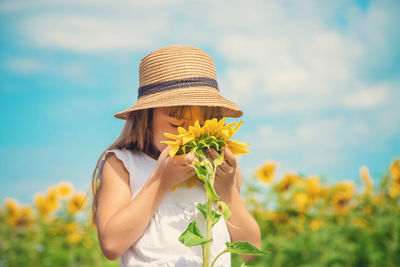 Girl wearing hat smelling sunflower