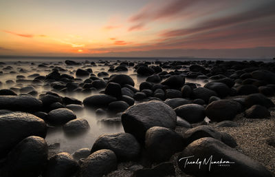 Rocks on beach against sky during sunset