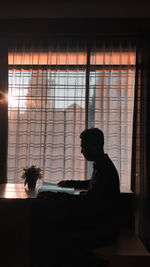 Silhouette people sitting by window at home