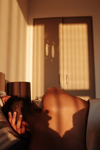 Rear view of shirtless man sleeping on bed during sunny day