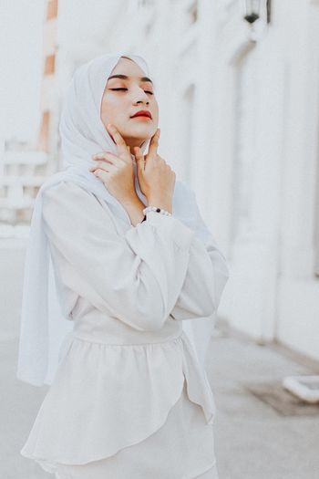 Beautiful young woman wearing hijab while standing against building