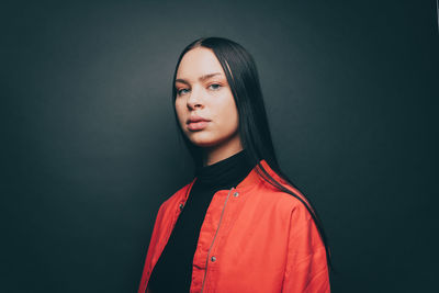 Portrait of woman wearing orange jacket over gray background