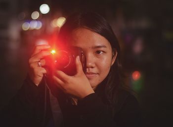 Close-up of young woman photographing with camera at night