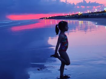 Woman standing on beach against sky during sunset