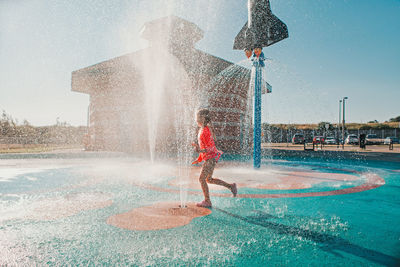 Funny girl playing on splash pad playground on summer day. happy child having fun in water. 