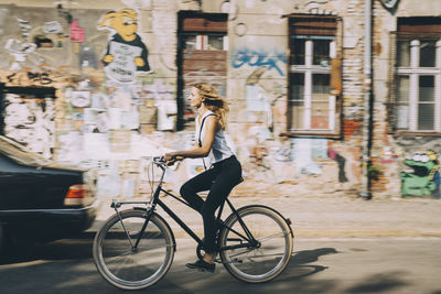 Side view of young businesswoman riding bicycle against building in city