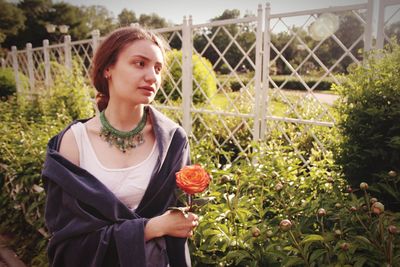 Portrait of young woman holding fruit against plants