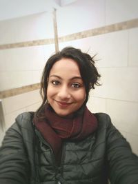 Portrait of smiling young woman standing against wall