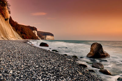Rocks on beach against sky during sunset