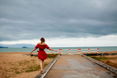 Woman walking on walkway at beach against sky