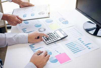 Cropped hands of man using calculator at table in office