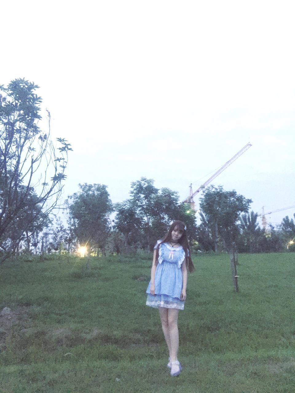 REAR VIEW OF WOMAN STANDING ON GRASSY FIELD AGAINST SKY