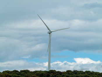 Low angle view of wind turbines on field against sky