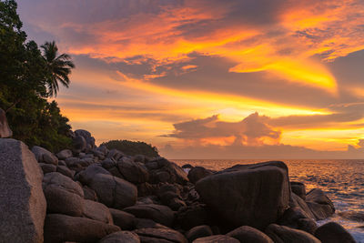 Rocks on beach against sky during sunset