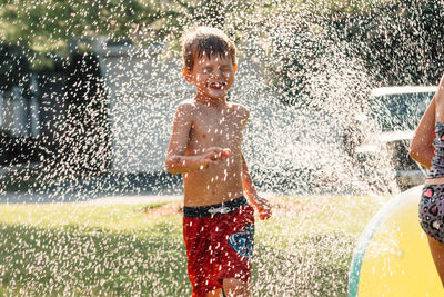 Water splashing on shirtless boy running in yard