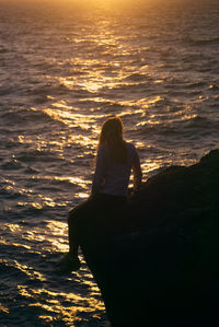 Rear view of woman sitting on beach during sunset