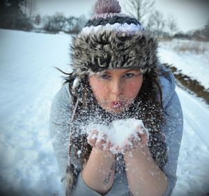 Close-up portrait of young woman blowing snow on field