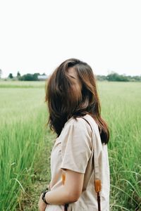 Woman covering face with brown hair standing amidst plants on field