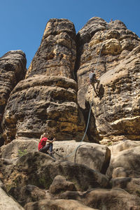 Rear view of man climbing on rock against sky