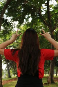 Rear view of woman with mobile phone standing against trees