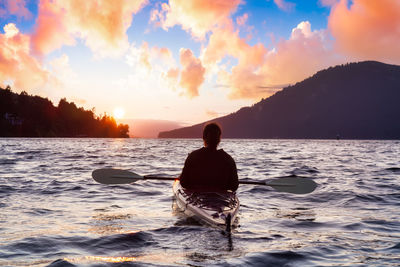 Rear view of silhouette man in sea against sky during sunset